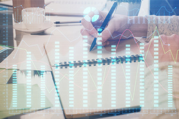 Forex chart hologram on hand taking notes background. Concept of analysis. Double exposure