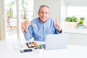 Handsome business senior man eating delivery sushi while working using laptop surprised with an idea or question pointing finger with happy face, number one