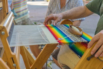 Man is weaving very fancy multi colored wool using a wooden loom.