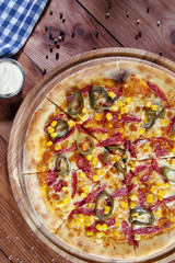 Top view hot chili pizza with corn, salami and red sauce on wooden background. Food flat lay. Copy space. Italian cuisine. Fresh homemade sliced pizza