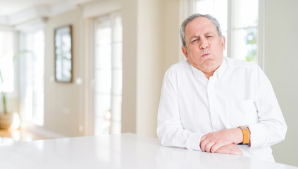Fototapeta premium Handsome senior man at home puffing cheeks with funny face. Mouth inflated with air, crazy expression.