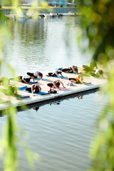 A big group of people attending yoga classes on a pontoon near the lake.