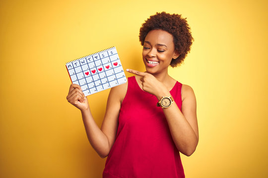 Young african american woman holding menstruation calendar over isolated yellow background very happy pointing with hand and finger