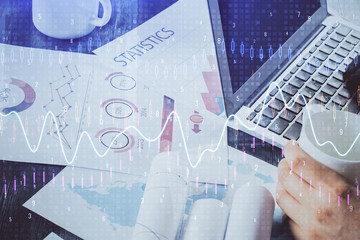 Double exposure of stock graph with businessman typing on computer in office on background. Concept of hard work.