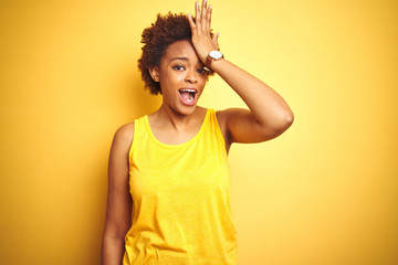 Beauitul african american woman wearing summer t-shirt over isolated yellow background surprised with hand on head for mistake, remember error. Forgot, bad memory concept.