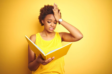 African american woman reading a book over yellow isolated background stressed with hand on head,...
