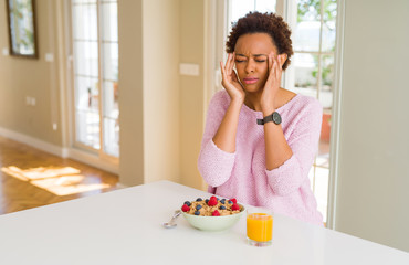 Young african american woman having healthy breakfast in the morning at home with hand on head for pain in head because stress. Suffering migraine.