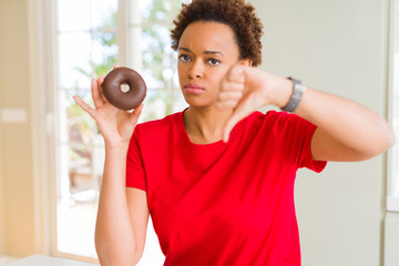 Young african american woman eating chocolate donut with angry face, negative sign showing dislike...
