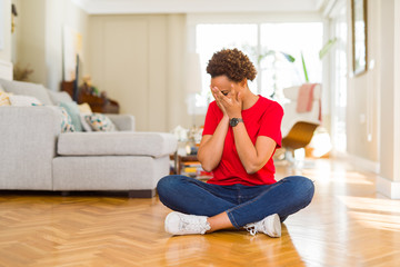 Young beautiful african american woman sitting on the floor at home with sad expression covering face with hands while crying. Depression concept.