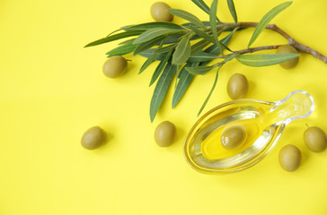 Flat lay olive oil in a glass in the form of olives and olive branch with green olives on a yellow...