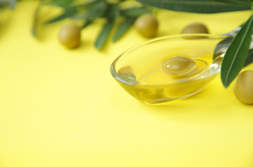 Close-up organic olive oil in a glass in the form of olives and olive branch with olives on a yellow wooden background. Ingredients. Healthy food. Mediterranean diet. Pattern, background, post card.
