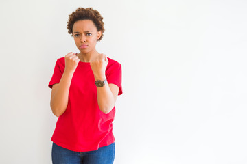 Young beautiful african american woman over white background Ready to fight with fist defense gesture, angry and upset face, afraid of problem