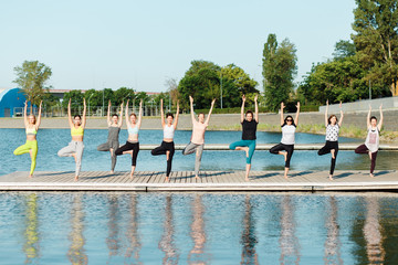 A big group of people attending yoga classes on a pontoon near the lake.