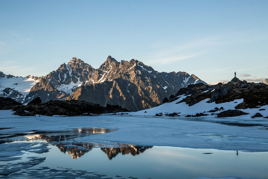Spring thaw on remote alpine lake in the Talkeetna Mountains of Alaska. Man standing on ridge reflected in the lake.