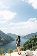 Naklejka premium A girl in a hat on the background of the sea and mountains admires a beautiful view of the natural landscape in Montenegro.