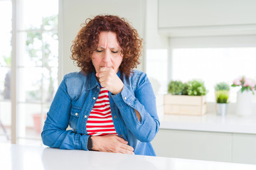 Middle age senior woman with curly hair wearing denim jacket at home feeling unwell and coughing as...