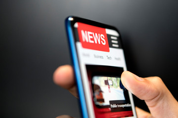 A man holding mobile smart phone with news on screen. Newspaper online portal in browser.