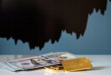 Gold bar, coins and a hundred-dollar bills on the background of the growth chart. Selective focus.