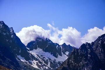 Horizontal beautiful panorama of the Caucasus mountains. The top of the mountain range covered with snow. Forest on the slope. Sunny day. Background image for travel and nature.