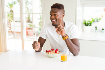 Young african american man eating healthy breakfast in the morning surprised with an idea or question pointing finger with happy face, number one
