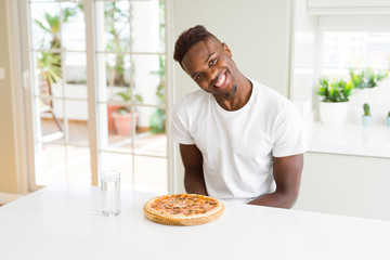 Handsome young african man holding and showing smiling proud homemade cheese pizza