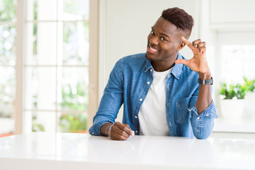 Handsome african american man at home smiling and confident gesturing with hand doing size sign with fingers while looking and the camera. Measure concept.