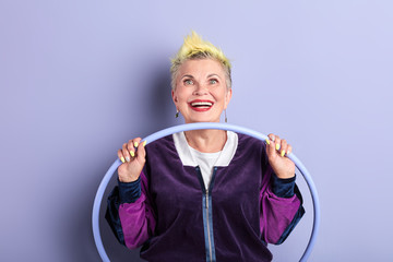 excited sporty mature woman holding hoop and posing to the camera. close up portrait, isolated violet background, fitness concept © alfa27