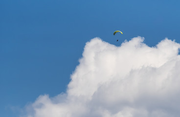 The lonely paraglider pilot flies against the background of the blue sky above clouds.  