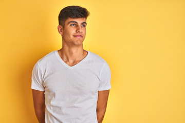 Obraz premium Young indian man wearing white t-shirt standing over isolated yellow background smiling looking to the side and staring away thinking.