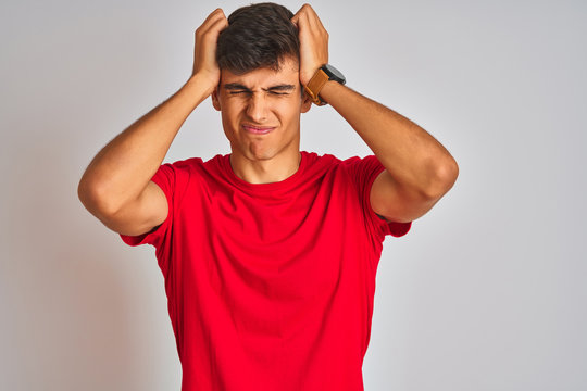 Young indian man wearing red t-shirt standing over isolated white background suffering from headache desperate and stressed because pain and migraine. Hands on head. - Powered by Adobe