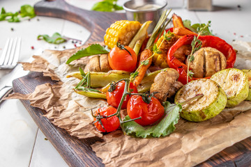 Vegan Grill menu, Grilled vegetables - zucchini, paprika, cherry tomatoes, corn, carrots and champignons served on wooden board at white background, horizontal orientation