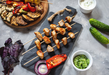 Assorted delicious grilled vegetables and chicken kebab on skewers on a concrete background. Summer barbecue.