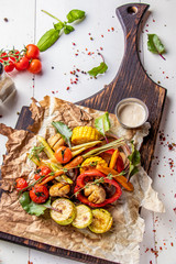 Vegan Grill menu, Grilled vegetables - zucchini, paprika, сherry tomatoes, corn, carrots and champignons served on wooden board at white background, vertical orientation