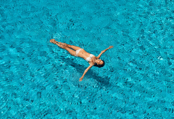 Top view of young slim woman in white bikini relax and floating in infinity swimming pool