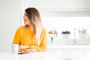 Young beautiful woman drinking a cup of coffee at home looking away to side with smile on face, natural expression. Laughing confident.