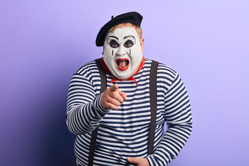 laughing crazy plump mime with wide open mouth points with finger at you, happiness, emotion and feeling. close up portrait, isolated blue background, studio shot