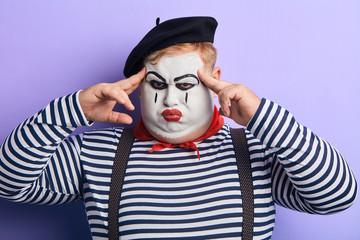 close up portrait of a theatrical actor with a make-up on his face touching his temples with...