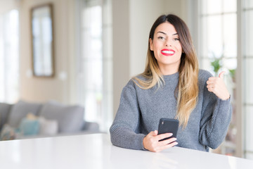 Young beautiful woman using smartphone at home pointing and showing with thumb up to the side with happy face smiling