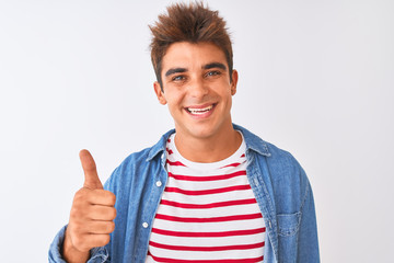 Fototapeta premium Young handsome man wearing striped t-shirt and denim shirt over isolated white background doing happy thumbs up gesture with hand. Approving expression looking at the camera with showing success.