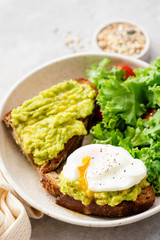 Avocado and poached egg on toasted rye bread served with kale and tomato salad. Closeup view of healthy food