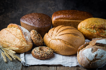 Assortment of fresh baked bread and buns on wooden table background