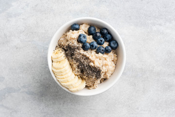Healthy Oatmeal Porridge In Bowl For Breakfast With Bananas Blueberry Chia Seeds. On Grey Concrete...