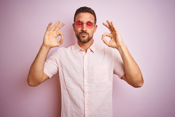 Handsome man wearing elegant summer shirt and sunglasses over pink isolated background relax and smiling with eyes closed doing meditation gesture with fingers. Yoga concept.