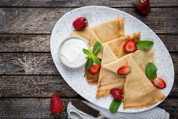 Crepes with strawberry and cream sauce. Homemade thin crepes for breakfast or dessert on wooden background, top view.