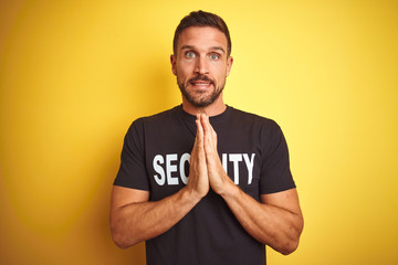 Young safeguard man wearing security uniform over yellow isolated background praying with hands...