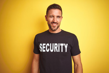 Young safeguard man wearing security uniform over yellow isolated background winking looking at the...