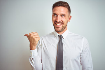 Young handsome business man wearing elegant white shirt over isolated background smiling with happy face looking and pointing to the side with thumb up.