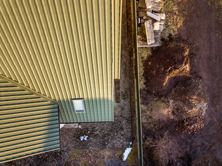 Aerial top view of green shingled house roof with new small attic plastic window.