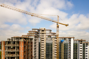 Apartment or office tall building under construction. Brick walls, glass windows, scaffolding and concrete support pillars. Tower crane on bright blue sky copy space background.