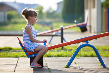 Cute young child girl outdoors on see-saw swing on sunny summer day.
